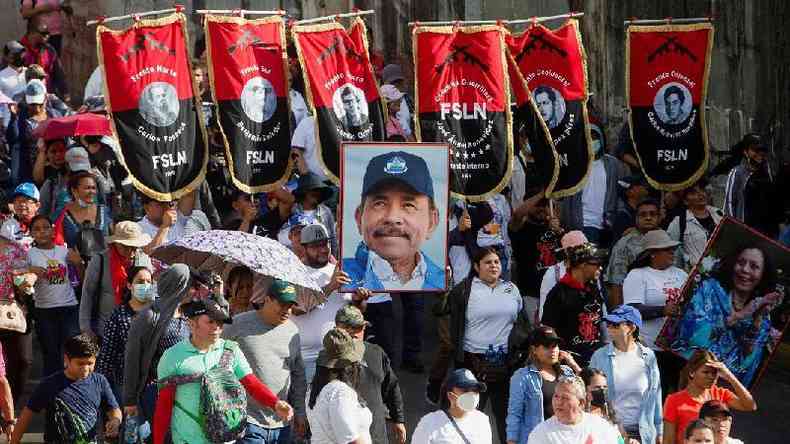 Vrias pessoas na rua, algumas segurando estandartes com sigla da FSLN e uma foto de Ortega