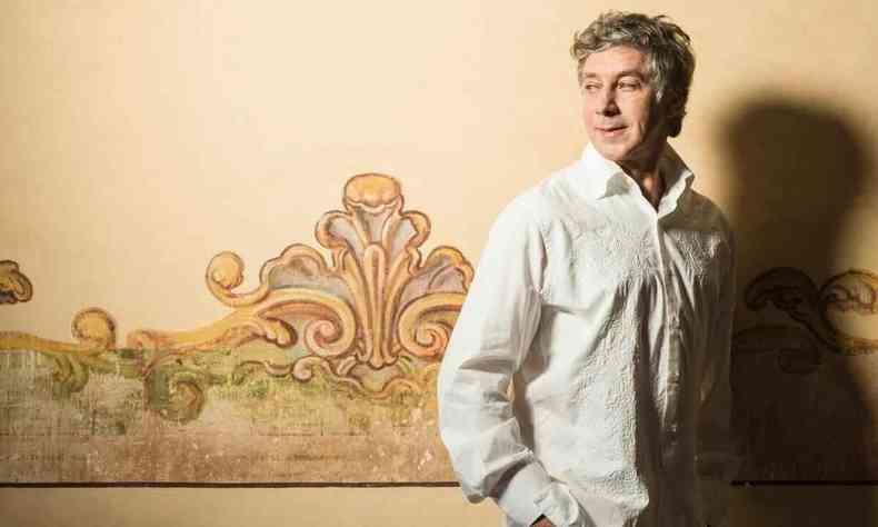 Cantor e compositor Flvio Venturini olha para atrs,  frente de parede amarela com pintura que remete ao barroco