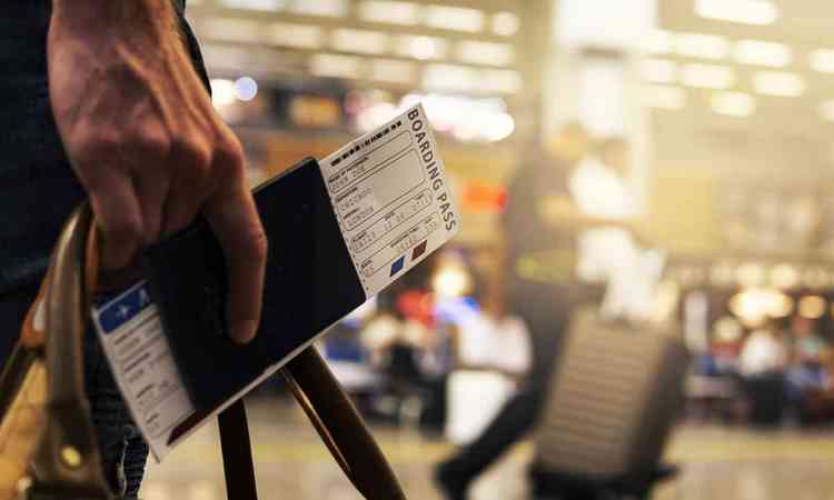 Imagem de uma pessoa segurando uma mala, um passaporte e uma passagem area