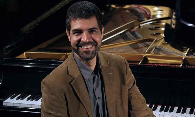 Andr Mehmari sorri, tendo um piano atrs de si