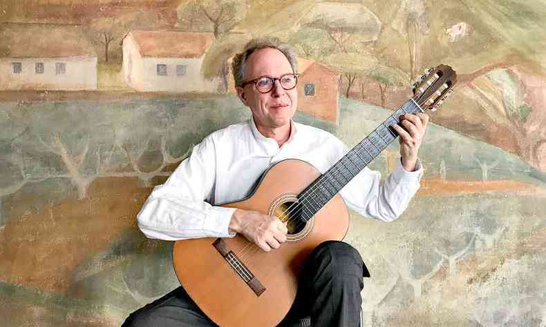 Com camisa branca, cala preta e culos de aros vermelhos, Arthur Nestrovski toca violo