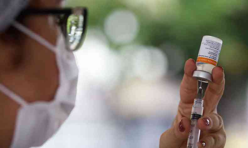 Profissional de sade com mscara branca insere seringa em frasco de vacina contra a COVID-19 para aplicar na populao