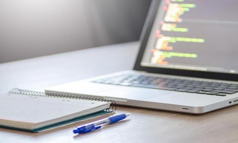 Computador aberto sobre a mesa, uma caneta e um caderno