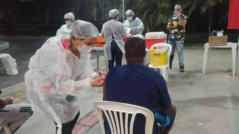 profissional da sade, usando equipamento de proteo, aplica dose de vacina em um morador