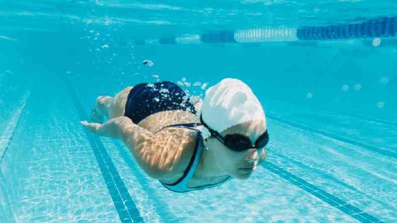 Mulher nadando em piscina debaixo d'gua