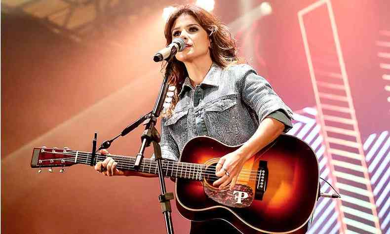 Usando casaco jeans, Paula Fernandes canta ao microfone e toca violo 