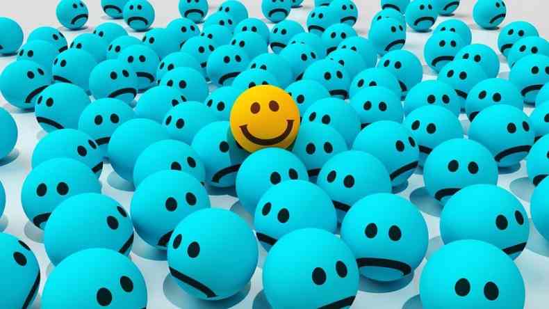 Emoji feliz em meio a dezenas de emojis tristes