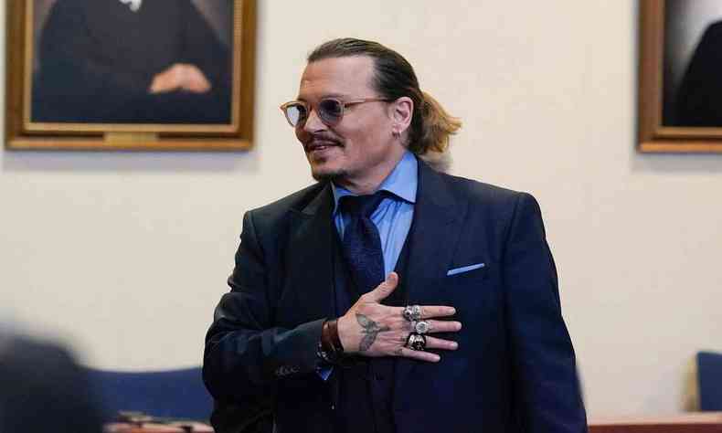 De rabo de cavalo e terno, Johnny Depp leva a mão ao peito