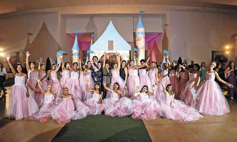 Grupo de debutantes participante do projeto Fadas Madrinhas posa para foto com roupas de baile cor-de-rosa. Atrs delas h um castelo de papelo 