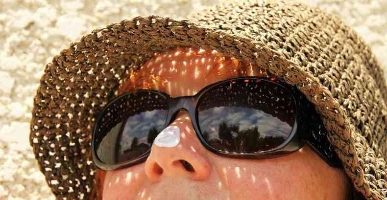 Mulher toma sol na praia com óculos e chapéu