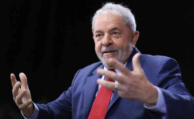 Lula est de terno azul e gravata vermelha; ele gesticula enquanto fala