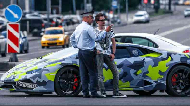Maksim Yakubets fala com policial em frente a um Lamborghini