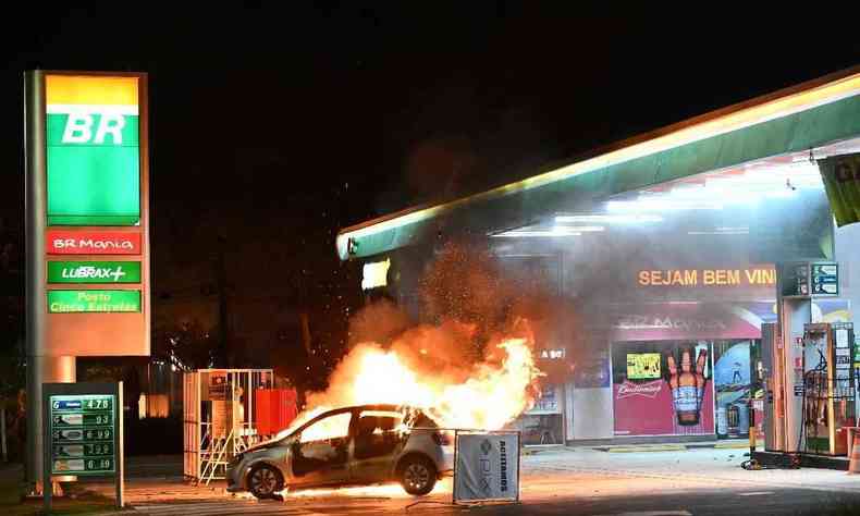 Carro pegando fogo em frente a um posto de gasolina  noite