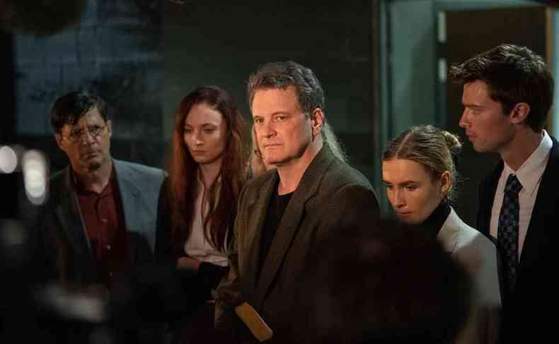 O ator Colin Firth, de pé, com semblante sério, cercado dos atores que interpretam seus filhos na série A escada