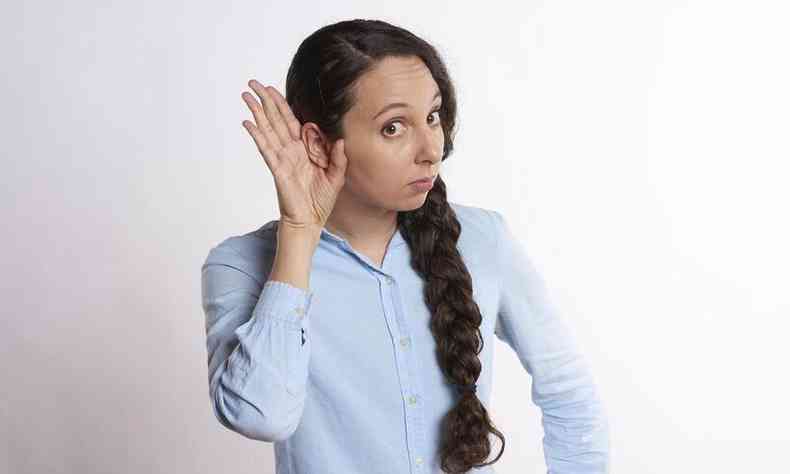 mulher com a mo no ouvido, fazendo o gesto para tentar ouvir