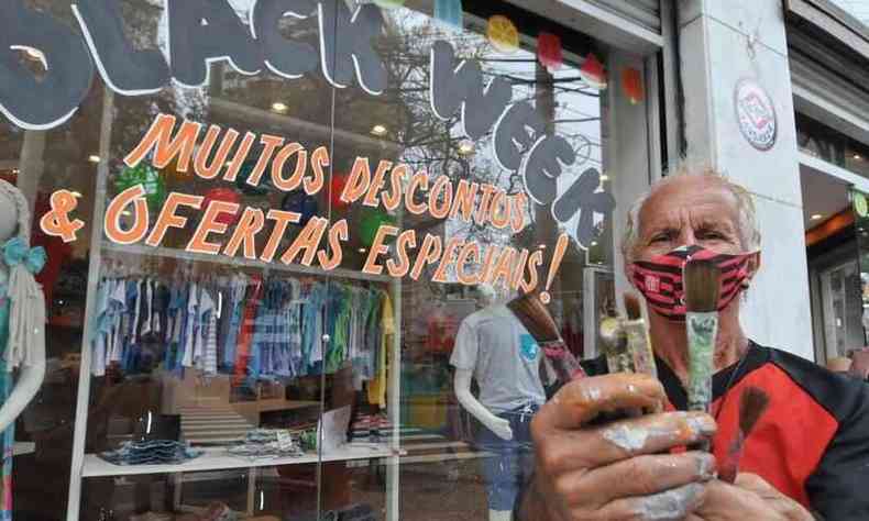 Pintor Gilson Silva, de 73 anos, segura os pincis com tinta usados para decorar a vitrine que est atrs dele; ele usa uma mscara de proteo nas cores e smbolo do Flamengo