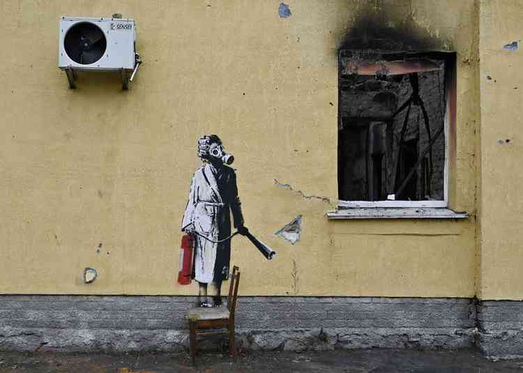 Grafite de Banksy em prdio de Kiev traz o desenho de mulher usando mscara. Ao lado est uma janela chamuscada pelo fogo