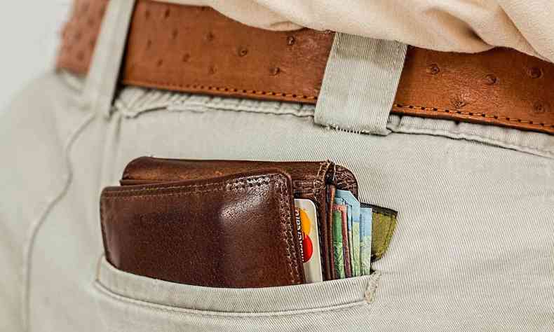 Bolso de uma pessoa em que aparece uma carteira com cartões e dinheiro