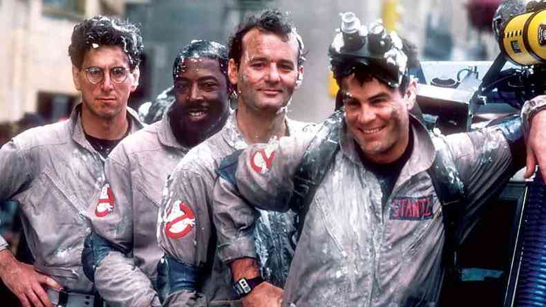 Os atores Rick Moranis, Ernie Hudson, Bill Murray e Dan Akroyd, de 'Caa-fantasmas', sorriem encostados em um carro