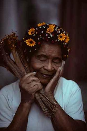 Mulher de olhos fechados e arranjo de flores nos cabelos segura flores secas junto ao rosto 