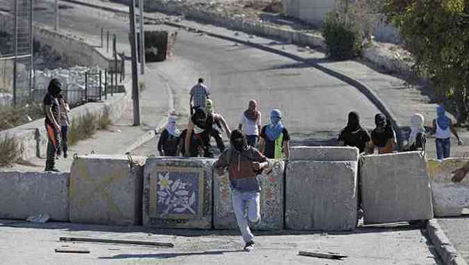 Jovem palestino mascarado atravessa bloqueio de concreto das foras israelenses(foto: AHMAD GHARABLI/AFP)