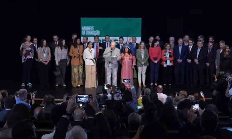 Lula e nomeados ministros em palco para coletiva de imprensa. Todos esto alinhados em uma fila para ficarem visveis para as cmeras e celulares que registram o momento