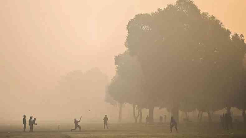 Pessoas jogando críquete em meio a uma poluição muito forte
