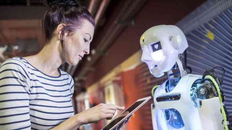 Mulher com tablet na mão em frente a um robô