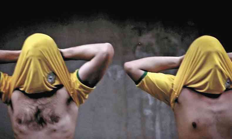 Dois homens cobrem o rosto com a camisa amarela da seleo brasileira e cruzam os braos atrs da nuca na instalao 'Morte sbita' (2014), de Jaime Lauriano