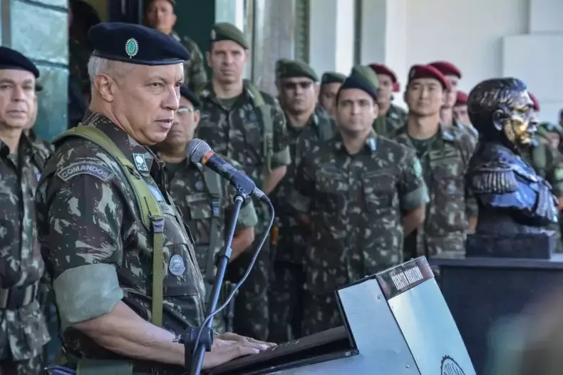 General de cabelos brancos e boina e roupam camuflada fala ao microfone observado por policiais tambm com roupas camufladas