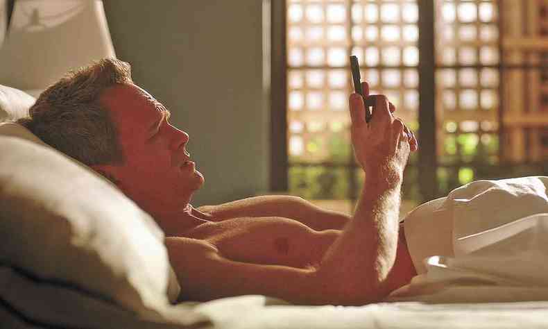 Neil Patrick Harris deitado na cama olha tela de celular com expresso preocupada em cena de uncoupled 