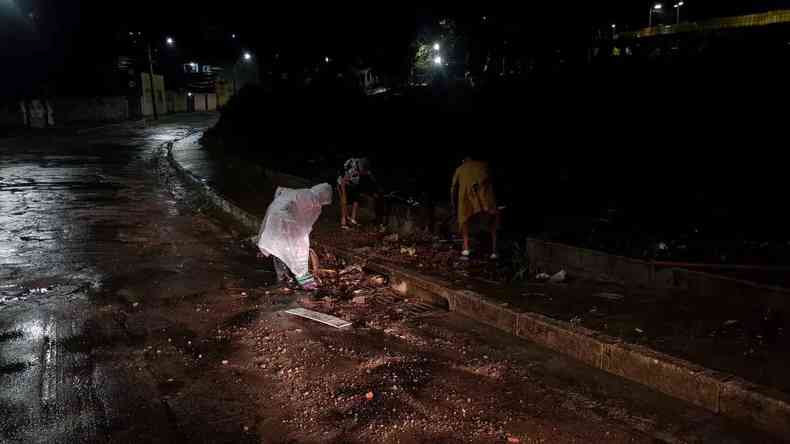 Trs moradores reunidos em uma rua do Bairro So Geraldo, em BH, para desentupir bueiro coberto de lixo e barro