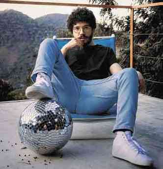 O cantor e compositor Octavio Cardozzo sentado numa varanda, com o p sobre um globo formado por espelhos, tendo ao fundo paisagem de montanhas