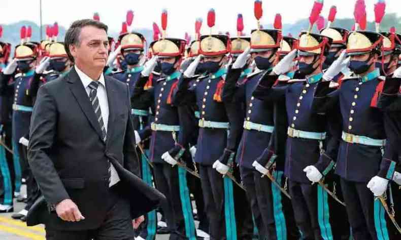 Bolsonaro, de terno preto, caminha ao lado de militares fardados