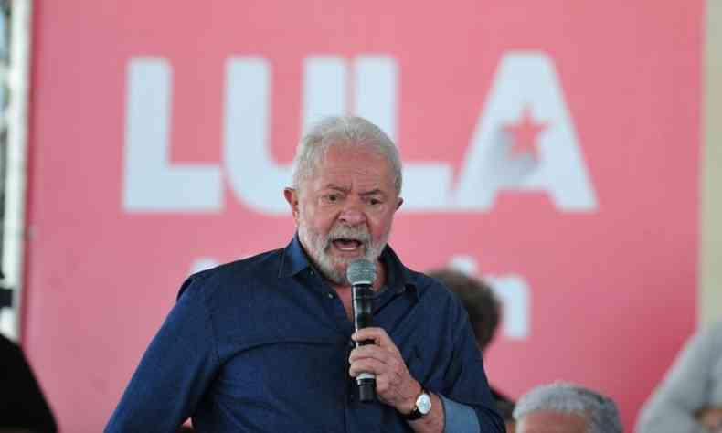 ex-presidente lula discursa ao microfone diante de um painel com seu nome