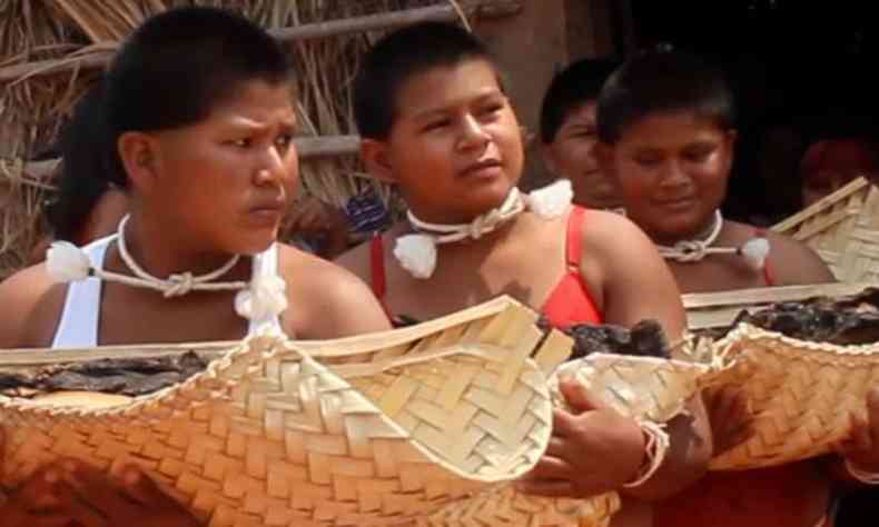 Indígenas carregam cestas de palha com folhas, em cena do filme dirigido por Divino Tserewahu