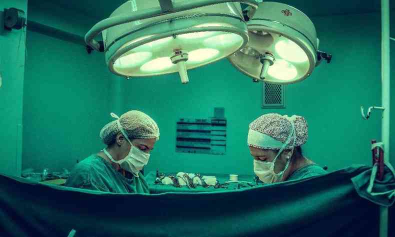 Centro cirúrgico onde dois médicos aparecem por trás de um lençol operando um paciente