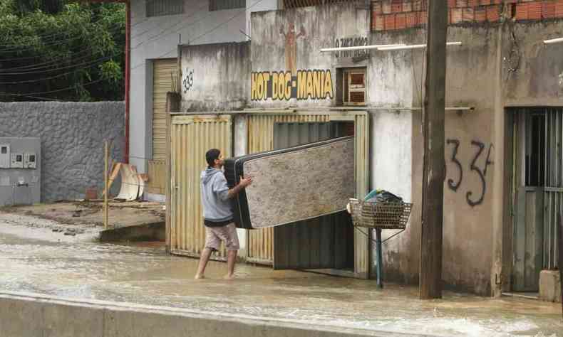 Homem carrega colcho para evitar estrago em inundao em Betim