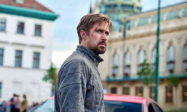 Ryan Gosling, de p, em rua, vestindo agasalho cinza e com traos de sangue no rosto em cena de agente oculto 
