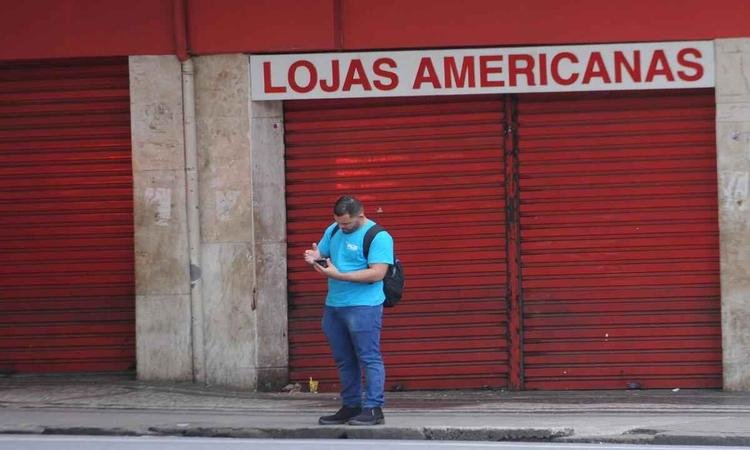 Homem utilizando celular em frente a varejista de portas fechadas