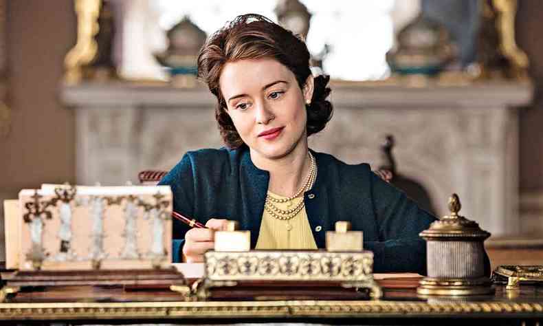 Claire Foy como a jovem Elizabeth II, sentada na escrivaninha, na serie The crown