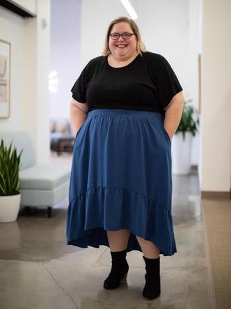 mulher loira, em p, gorda, de blusa preta e saia azul