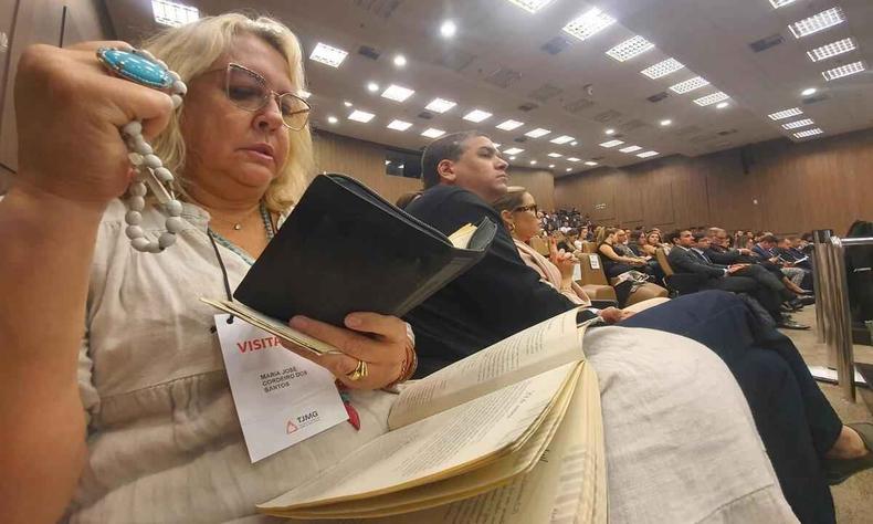 uma mulher de cabelo loiro segurando um tero e uma bblia. Ela est com uma roupa mais clara 