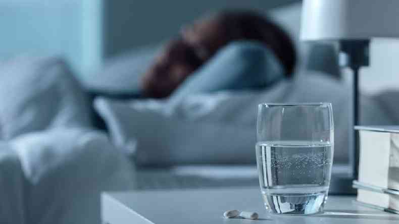 Pessoa dormindo; em primeiro plano, um copo com gua e um comprimido