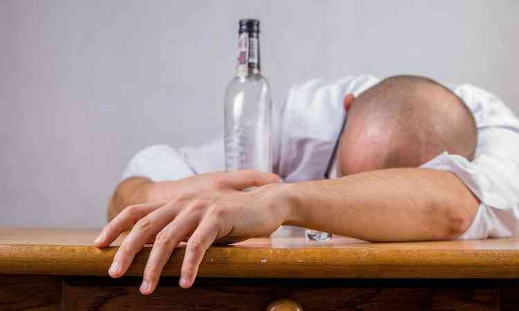 homem deitado sobre mesa, com litro de bebido ao lado