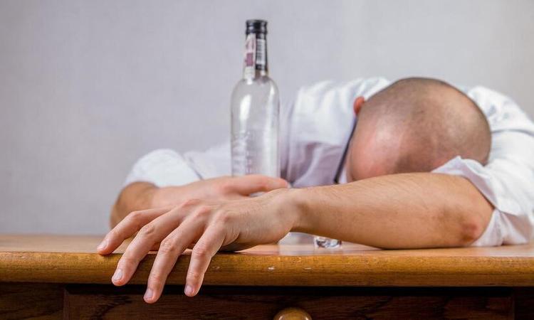 homem deitado sobre mesa, com litro de bebido ao lado