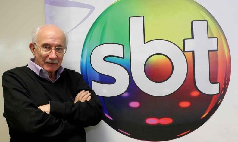 Reynaldo Boury olha para a cmera, tendo atrs de si o logotipo do SBT