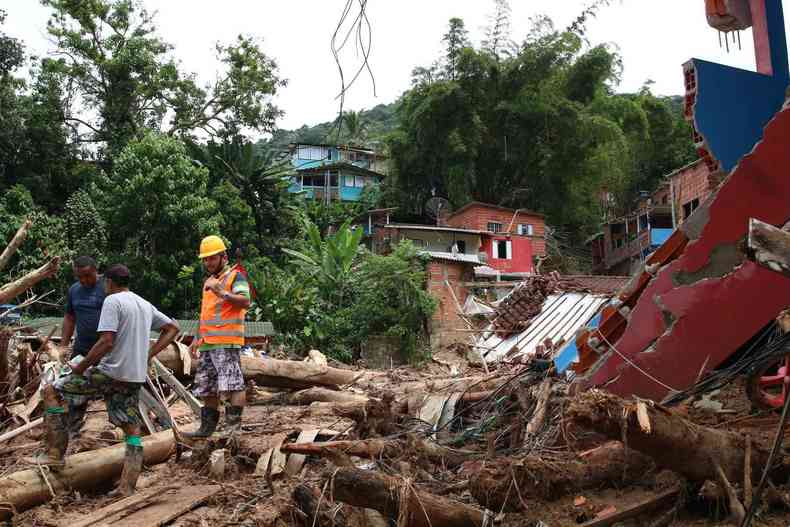 Homens em rea totalmente destruda; com lama e destroos das casas 