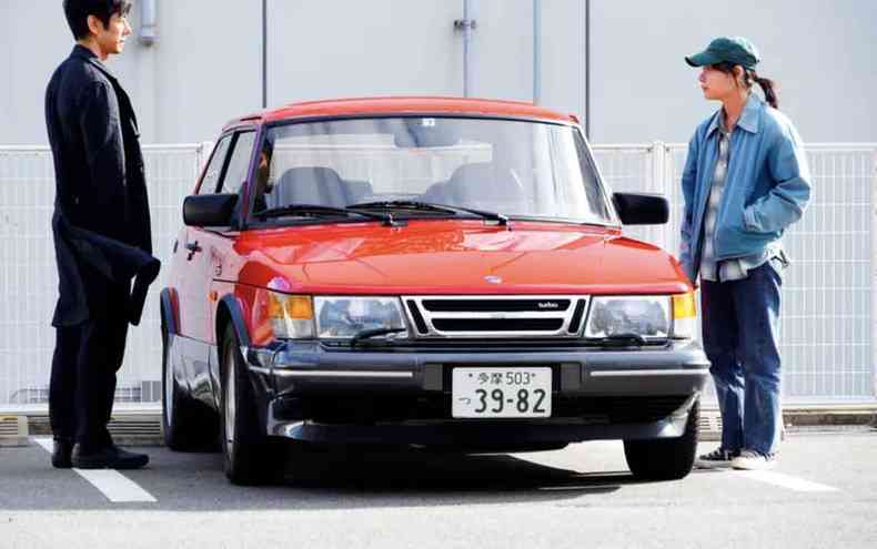 Atores Hidetoshi Nishijima e Toko Miura olham para um carro vermelho, no filme Drive my car