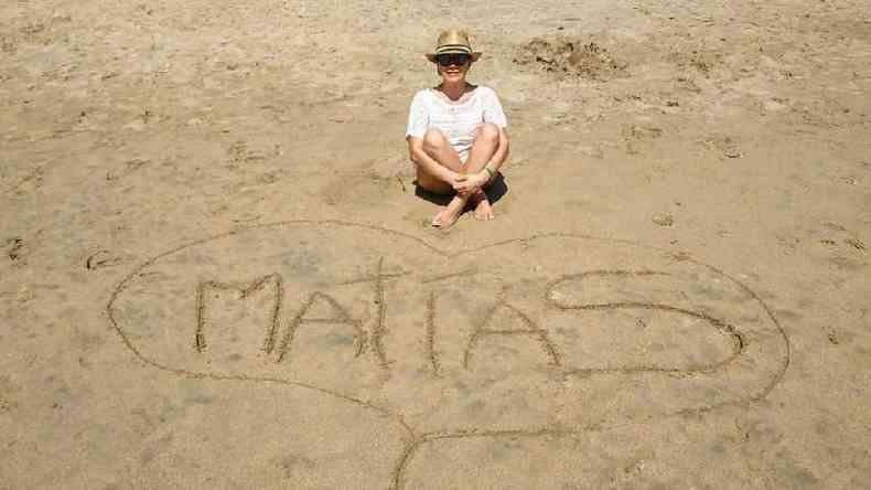 Ileana Garca Mora sentada na praia em frente ao nome de seu filho, Matas